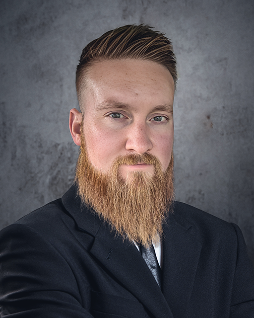 Man with a beard wearing a dark suit against a gray background